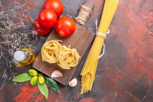 Top view raw pasta with oil tomatoes and garlic on dark surface raw pasta dough