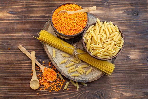 Top view raw pasta with orange lentils on brown surface