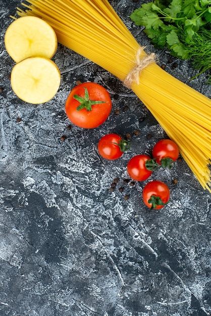 Vista dall'alto di pasta cruda con patate, prezzemolo e pomodori su superficie grigio chiaro