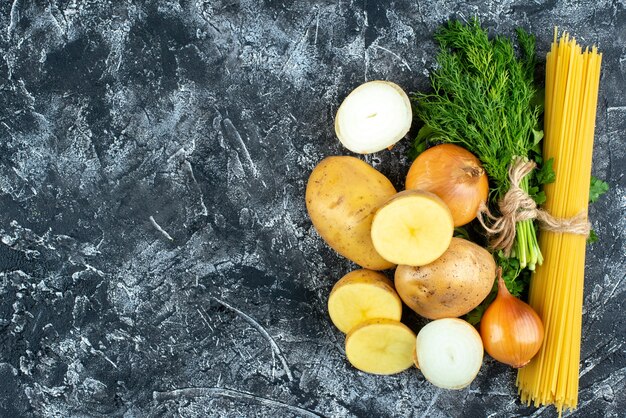 Top view of raw pasta with potatoes, parsley and onions on light gray surface