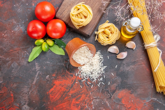 Top view raw pasta with rice and red tomatoes on dark surface pasta dough raw