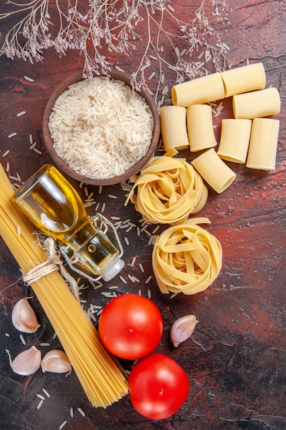 Top view raw pasta with rice and tomatoes on the dark surface dough pasta raw