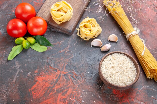 Top view raw pasta with rice and tomatoes on a dark surface pasta dough raw