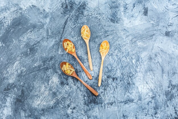 Top view raw pasta in wooden spoons on grey plaster background. horizontal