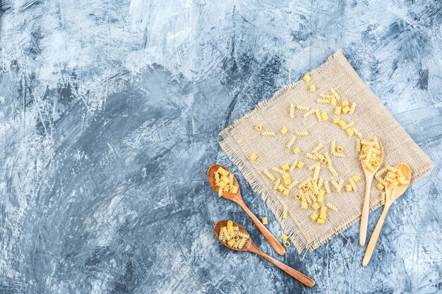 石膏と袋の背景に木のスプーンで生パスタの上面図。水平