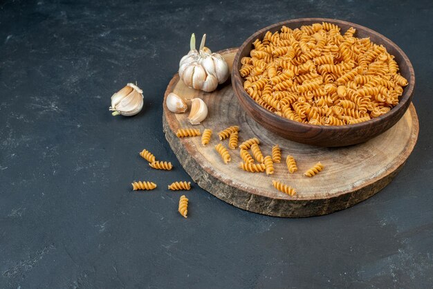 Top view of raw pastas inside and outside brown pot garlics on dark color background