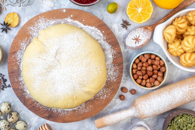 Top view of raw pastry on round wooden board grater and lemon hazel-nuts on ice background