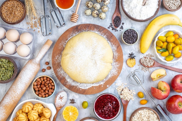 Top view of raw pastry on round wooden board grater and set of foods on ice background