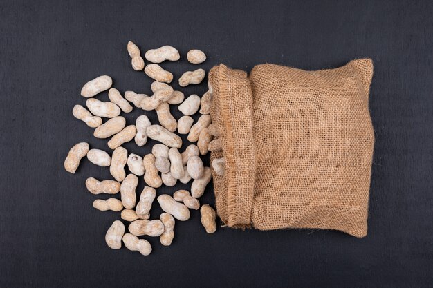 Top view raw peanuts in sack on dark 