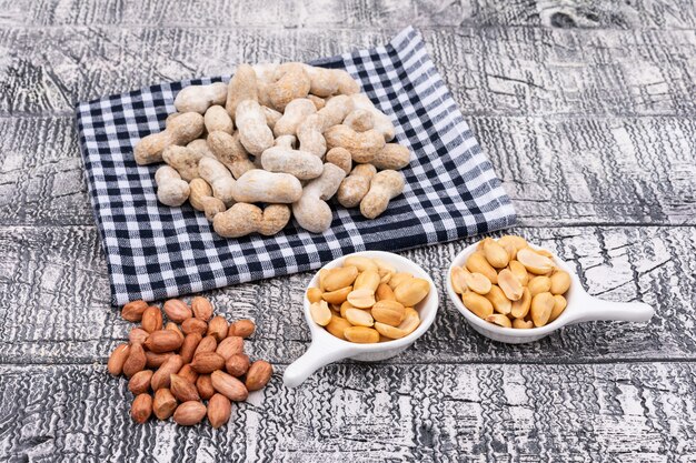 Top view raw peanuts on table cloth and in plates on wooden 