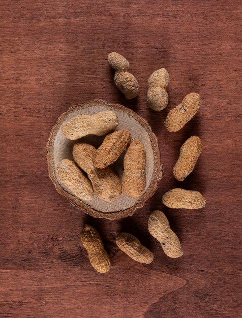 Top view raw peanuts on wooden stand on brown