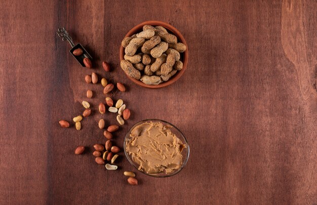 Top view raw and peeled peanuts in bowl and peanut butter on wooden  horizontal