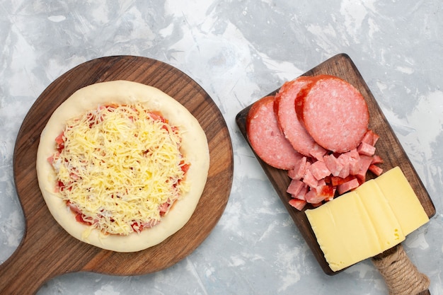 Top view raw pizza with cheese and sausages on light white