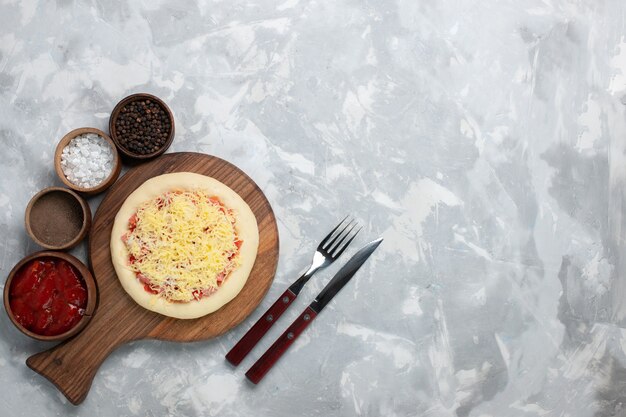 Pizza cruda vista dall'alto con formaggio e condimenti sulla scrivania bianca