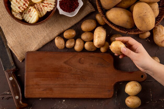 Top view raw potatoes in a basket and sliced potatoes with dried chili flakes in bowl on brown background