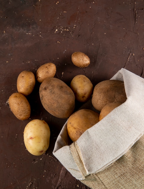 Бесплатное фото Вид сверху сырой картофель в сумке на коричневом фоне