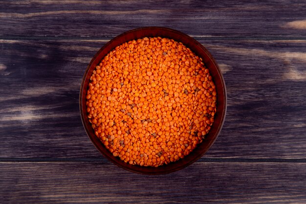 Top view of raw red lentils in a wooden bowl on purple rustic background