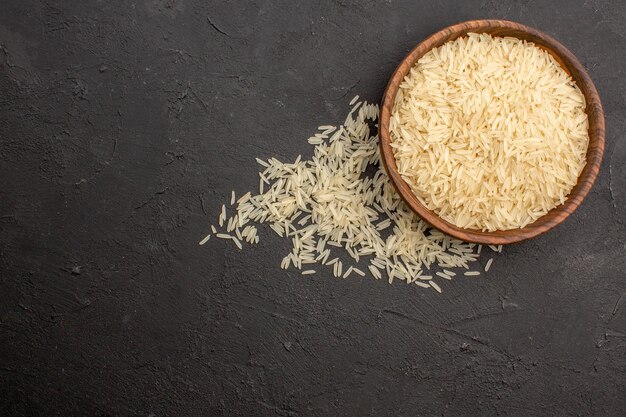 Top view of raw rice inside brown plate on dark grey surface