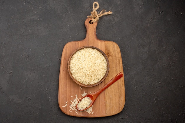 Top view of raw rice inside wooden brown plate on grey surface