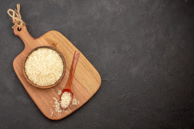 Top view of raw rice inside wooden brown plate on the grey surface