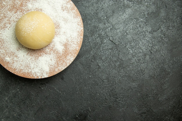 Top view raw round dough with flour on the dark grey desk dough raw meal flour food