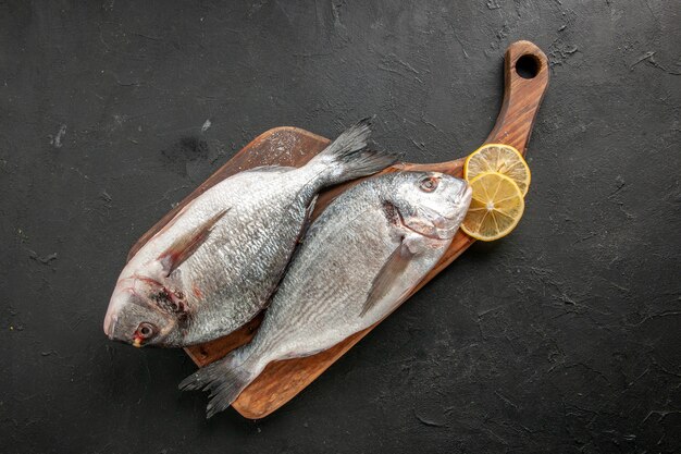 Top view raw sea fish lemon slices on chopping board on black