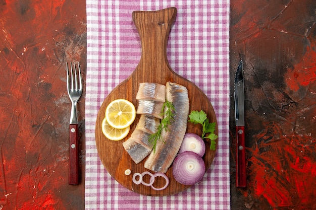 Top view raw sliced fish with onion rings and lemon on dark background