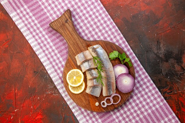 Top view raw sliced fish with onion rings and lemon on dark background