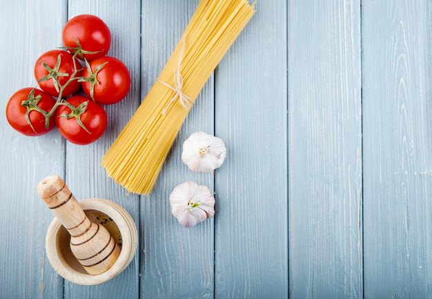 Вид сверху сырых спагетти, перевязанный веревкой со свежими помидорами, чесноком и деревянной ступкой с копией пространства на деревенском фоне