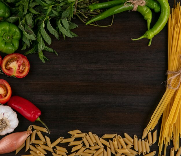 Top view of raw spaghetti with pasta tomatoes bell pepper and garlic with mint on a wooden surface