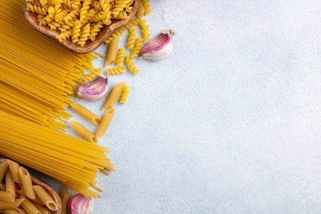 Top view of raw spaghetti with raw pasta in bowls with garlic on a gray surface