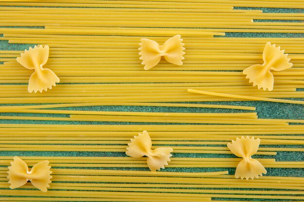 Top view of raw spaghetti with raw pasta on a green surface