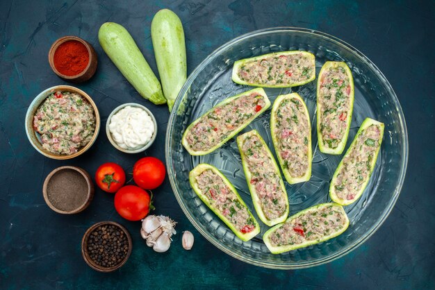 Top view of raw squashes with spicy minced meat inside glass plate on the dark blue surface