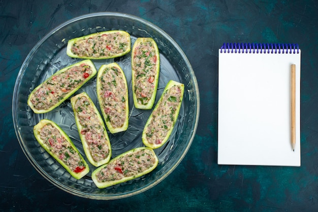 Top view of raw squashes with spicy minced meat inside glass plate on the dark blue surface