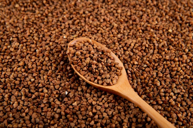 Top view of raw uncooked buckwheat in a wooden spoon on the surface fully covered with buckwheat