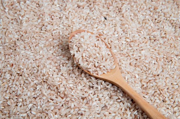 Top view of raw uncooked white rice in a wooden spoon on the surface fully covered with raw rice