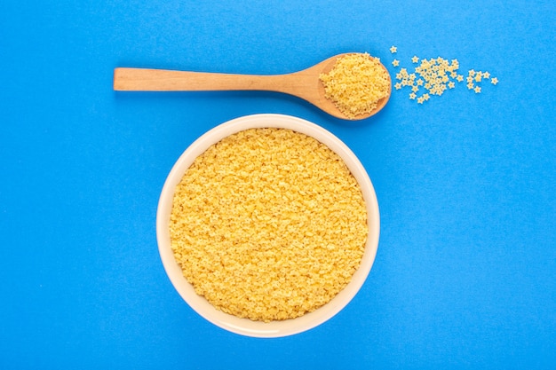 A top view raw yellow pasta inside white bowl along with brown wooden spoon isolated on the blue background food meal spaghetti