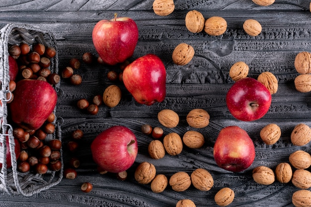 Вид сверху красные яблоки в корзине с орехами и грецкими орехами на серой деревянной горизонтали