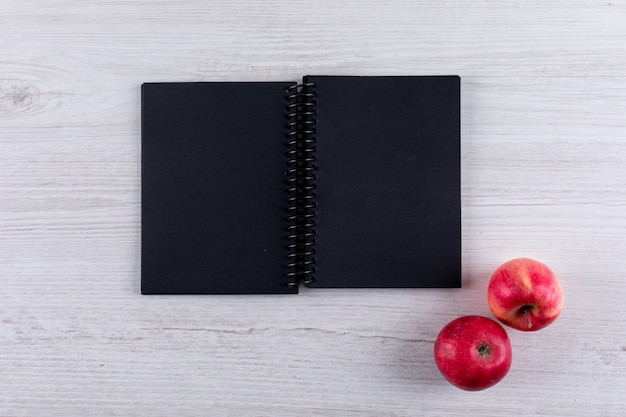 Free photo top view red apples with copy space on black notebook on white wooden  horizontal