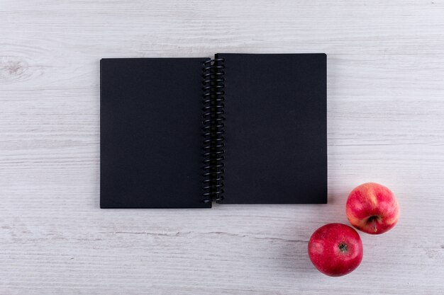 白い木製の水平に黒いノートにコピースペースを持つトップビュー赤いリンゴ