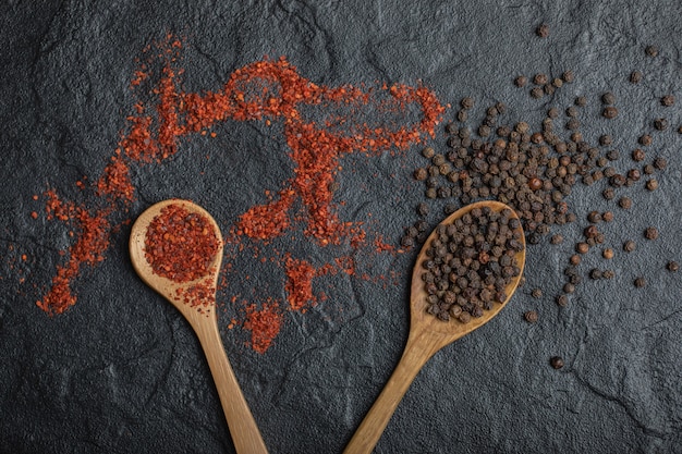 Free photo top view of red and black peppercorns with wooden spoon over black background. close up photo.