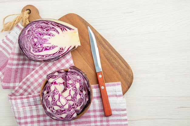 Top view red cabbage in bowls on purple white checkered kitchen towel knife on cutting board on grey table