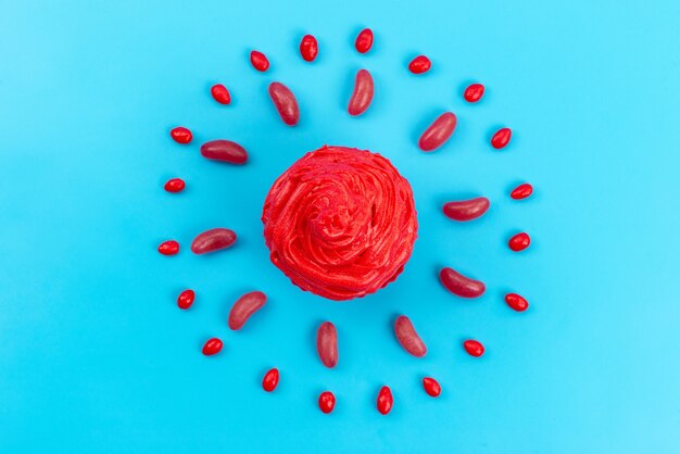 A top view red cake with red candies spread all on blue, biscuit color cake