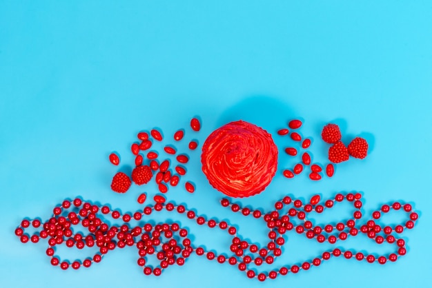 A top view red cake with red candies spread all on blue desk, biscuit color candy