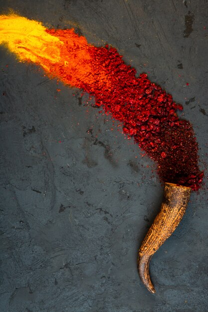 Top view of red chilli and sumac powder spices with curry scattered from a horn on black