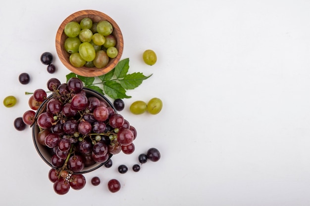 Вид сверху красного винограда и белых виноградных ягод в мисках с виноградными ягодами и листьями на белом фоне с копией пространства