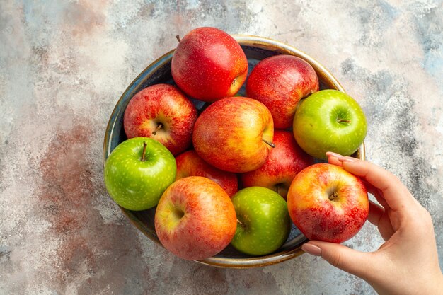 Top view red and green apples in bowl apple in female hand on nude surface