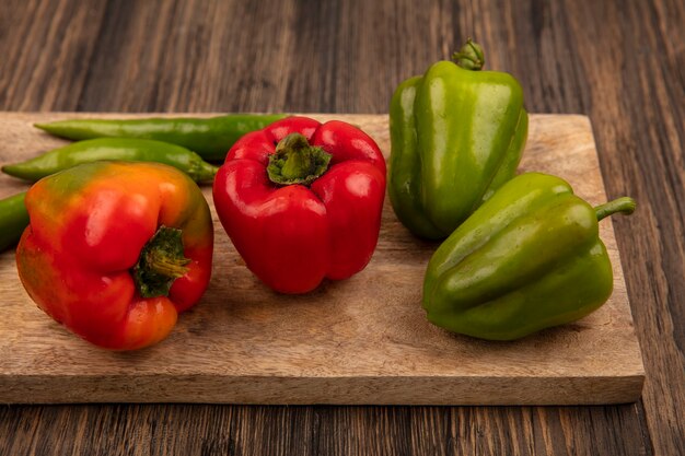 Top view of red and green bell peppers on a wooden kitchen board on a wooden background