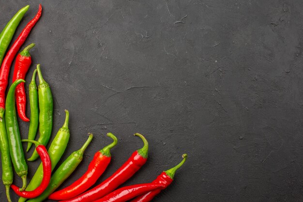 Top view red and green peppers at the bottom left of black table with free space