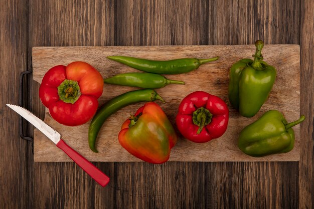 Top view of red and green peppers on a wooden kitchen board with knife on a wooden surface